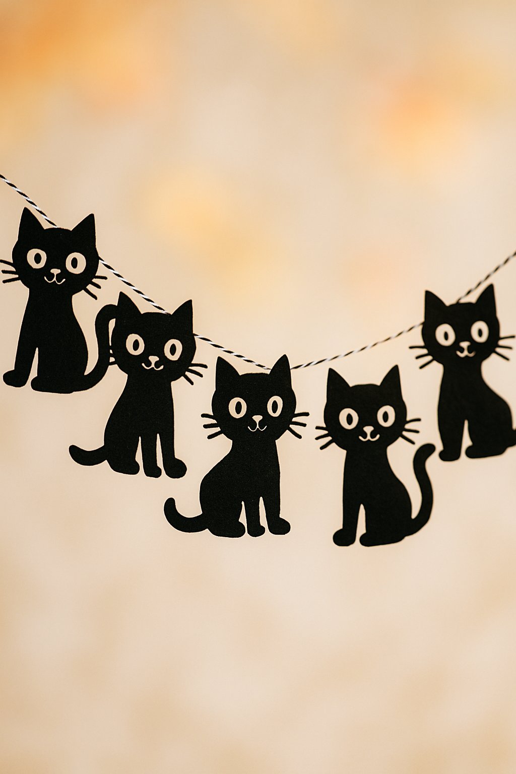 A string of six black cat-shaped decorations hanging against a neutral background.